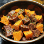 Slow cooker beef stew with pumpkin chunks, garnished with fresh herbs, served in a black bowl. Perfect comfort food for cozy dinners or meal prep. Delicious and hearty homemade beef stew recipe.