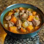 Savory beef and vegetable stew with tender chunks of meat, carrots, potatoes, and herbs, served in a rustic bowl for a hearty homemade meal.