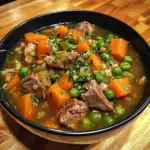 Slow cooker beef stew with carrots, peas, and fresh herbs in a black bowl on wooden table.