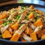 Roasted chicken with sweet potatoes, green peas, quinoa, and fresh herbs in a black skillet for healthy dog food.