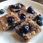 Blueberry oatmeal bars with fresh blueberries on white plate, healthy homemade blueberry oatmeal snack, baked oatmeal bars with blueberries and nuts, dessert recipe by Waggy Chef.