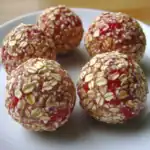 Sweet oatmeal balls with red berry filling coated in oats on a white plate for healthy, tasty treats. Perfect for snack or dessert, easy to make at home with simple ingredients.