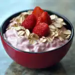 Fresh strawberry yogurt with rolled oats and sliced strawberries in a red bowl, healthy breakfast or snack option.