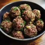 Quinoa and beef meatballs garnished with fresh herbs in a black bowl, healthy gluten-free vegan appetizer or main dish, delicious protein-packed meal with colorful ingredients.
