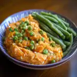 Mashed sweet potatoes with green peas and garlic in a blue ceramic bowl, healthy vegan comfort food, nutritious side dish, colorful and appealing presentation, Waggy Chef selection.