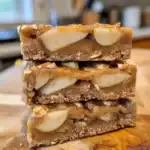 Homemade caramel apple granola bars with sliced apples, oats, and honey on a wooden surface. Perfect healthy snack featuring chewy texture and natural sweetness.