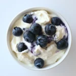 Fresh blueberries on creamy yogurt, healthy snack or breakfast option, top view.