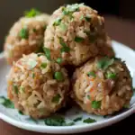 Savory rice and vegetable meatballs on white plate, garnished with chopped herbs, close-up shot, healthy vegan snack, flavorful Asian-inspired dish, Waggy Chef recipe.