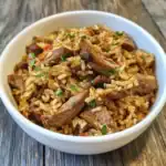 Juicy beef stir-fried rice in a white bowl, garnished with fresh herbs, served on rustic wooden table. Perfect for homemade dog food or tasty pet meals.