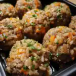Savory rice and meatloaf-style meatballs with vegetables, garnished with chopped parsley, served in a black tray for meal prep or takeaway.
