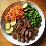 Juicy grilled beef steak with fresh zucchini, green peas, quinoa, and roasted vegetables on a white plate. Perfect healthy meal for dog lovers and food enthusiasts.