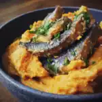 Freshly cooked fried fish served over mashed sweet potatoes, garnished with chopped herbs in a black bowl, highlighting a flavorful, nutritious dish.