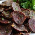 Delicious homemade beef jerky with spices and herbs on a white plate, served with fresh parsley. Perfect for snack lovers and pet owners seeking healthy, protein-rich treats.