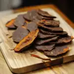 Crispy beef jerky snacks on wooden cutting board, dried and seasoned pet treat, healthy dog treats, Waggy Chef pet snack, high-protein dog food supplement.