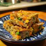 Quinoa vegetable casserole with carrots, peas, and herbs, baked to golden perfection on a blue ceramic plate, showcasing a healthy, delicious plant-based meal option for nutritious eating.