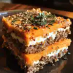 Roasted butternut squash lasagna with quinoa, ricotta, and herbs on a black plate. Healthy, gluten-free, plant-based, vegetarian dish with vibrant orange squash and fresh herbs. Perfect for vegan meal prep.
