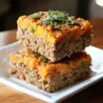 Ground beef and sweet potato casserole topped with cheese and fresh herbs, served on a white plate.