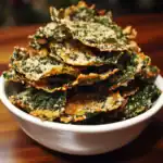 Crispy kale chips with grated cheese, a healthy snack or appetizer, served in a white bowl on a wooden surface. Perfect for crunchy, nutritious treats.