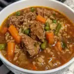 Savory beef stew with tender meat, carrots, green peas, and rice in flavorful broth, perfect for comforting home-cooked meals.