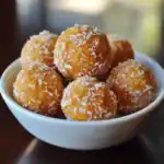 Sweet, golden coconut balls or ladoos coated with shredded coconut in a white bowl, perfect for Indian desserts and festive celebrations.