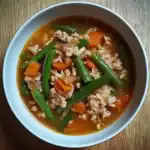Fresh homemade ground beef and vegetable stir-fry in savory broth, featuring green beans, carrots, and minced beef, served in a white bowl for a nutritious meal.