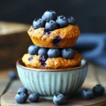 Fresh blueberry muffins topped with ripe blueberries in a ceramic bowl, showcasing a delicious homemade dessert perfect for breakfast or snack.