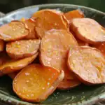 Sweet potato slices garnished with sea salt served on a dark green ceramic plate for healthy, flavorful snack options.