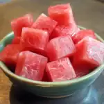 Juicy watermelon cubes in a small green bowl, fresh fruit snack, summer refreshment, vibrant pink color, healthy hydration, perfect for picnics and hot days, ripe and sweet, ready to eat.
