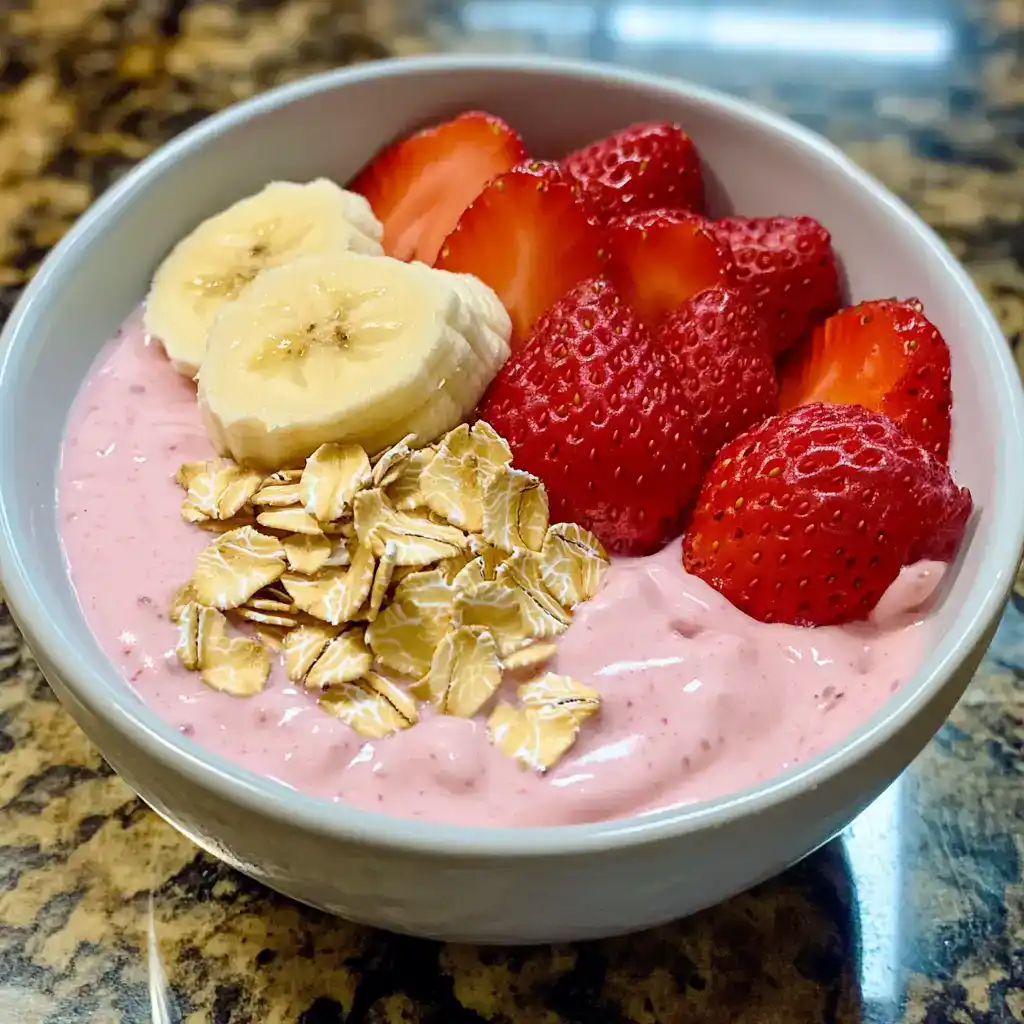 Fresh strawberry and banana smoothie bowl topped with sliced strawberries, banana slices, oats, and granola on a white bowl, healthy fruit breakfast, colorful and nutritious snack, Waggy Chef image.
