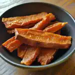 Sweet potato fries with crispy edges and caramelized coating, served in a black bowl, perfect for pet treats or healthy snacks. Great for dogs and pet nutrition.