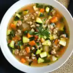 Savory vegetable and ground turkey soup with zucchini, carrots, onions, and fresh herbs in a white bowl.