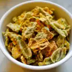Dried green beans with seasoning in a white bowl, suitable for pet treats or healthy snacks, displayed on a neutral background.