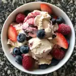 Fresh mixed berries and vanilla ice cream in a white bowl, perfect for a summer dessert.