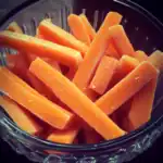 Fresh cut carrot sticks with a salted, frosty appearance in a glass bowl, perfect for healthy snacks or pet treats.
