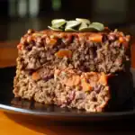 Crumbled meatloaf with vegetables and pumpkin seeds on top, served on a black plate, close-up view.