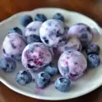 Fresh frozen blueberries with creamy yogurt coating on a white ceramic plate, perfect for healthy snacks or smoothies.