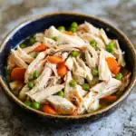 Shredded chicken with peas and carrots in a black bowl, healthy homemade dog food recipe, Waggy Chef, nutritious pet meal, natural dog food options, high-quality ingredients for dogs.