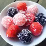 Fresh strawberries and blackberries covered with shredded coconut on a white plate, perfect for healthy snacks or desserts.
