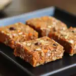 Sweet vegan granola bars with oats, nuts, and dried fruits on a black tray.