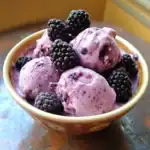 Creamy blackberry ice cream with fresh blackberries in a decorative bowl, perfect for summer dessert or a refreshing treat.