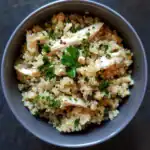 Fluffy cooked quinoa salad with shredded chicken, fresh parsley, and herbs in a bowl, healthy gluten-free vegan recipe, nutritious and colorful grain dish.
