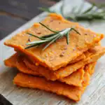 Golden sweet potato dog treats stacked on a wooden board garnished with fresh rosemary for healthy homemade pet snacks. Perfect for dogs, delicious, nutritious, and easy to make.