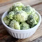 Creamy broccoli florets with cheese in a white bowl, garnished with grated cheese, served on a rustic wooden table for healthy, delicious vegetable side dish.