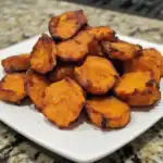 Golden roasted sweet potatoes on a white plate, perfectly cooked with crispy edges, served as a healthy and delicious snack or side dish.