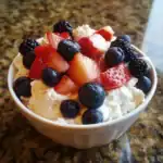 Fresh mixed berry fruit salad with strawberries, blueberries, blackberries, and whipped cream in a white bowl. Perfect healthy dessert or snack for all ages.
