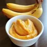 Creamy banana puree in a white bowl with fresh bananas in the background, perfect for healthy dog treats or homemade pet foods. Nutrient-rich and delicious for your furry friend.