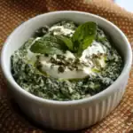 Creamed spinach dip with fresh herbs and garnishes in a white ramekin, close-up, appetizing healthy side dish for dinner or lunch, garnished with mint leaves and grated cheese, perfect for gourmet meals and vegetable lovers.
