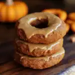 Rich cinnamon apple donuts stacked on a wooden surface with pumpkins in the background, perfect for fall treats.