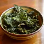 Crispy kale chips in a ceramic bowl, healthy snack made from baked kale leaves, vibrant green color, food photography, Waggy Chef, vegan and gluten-free snack options, perfect for wellness and nutrition enthusiasts.