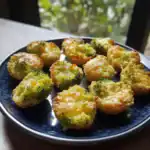 Crispy baked broccoli bites topped with melted cheese, served on a dark plate, perfect for healthy snacking or appetizer, showcased with natural sunlight.